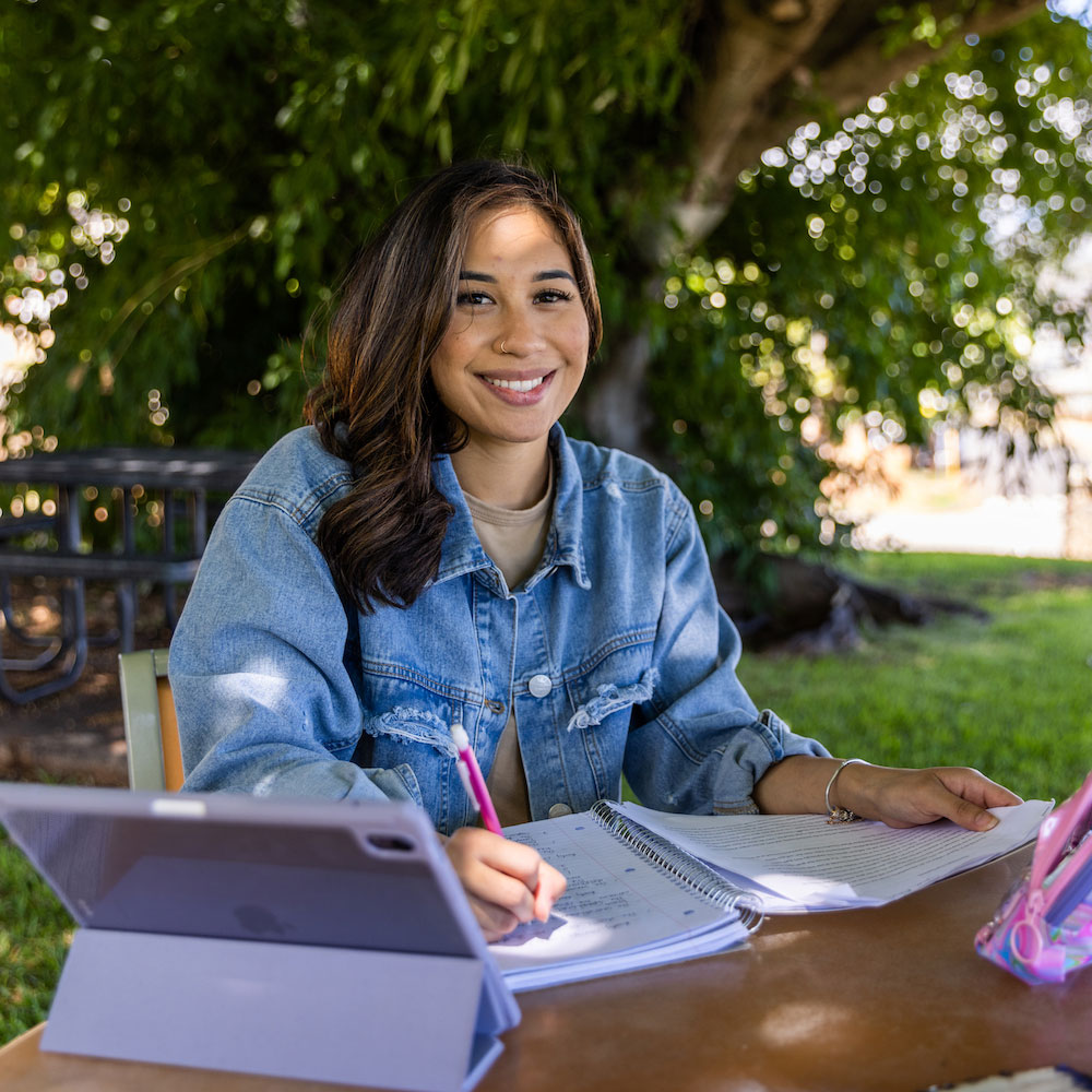 Student sitting outdoors using a laptop and writing notes